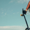 Skateboarder performing an ollie in the air on a skateboard with a clear blue sky and palm trees in the background.
