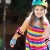 Young girl wearing a colorful helmet, elbow and wrist pads, roller skating outdoors while smiling and enjoying a sunny day.